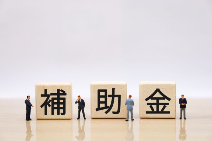 「補助金」と書かれた木製ブロックと検討する人々のミニチュア